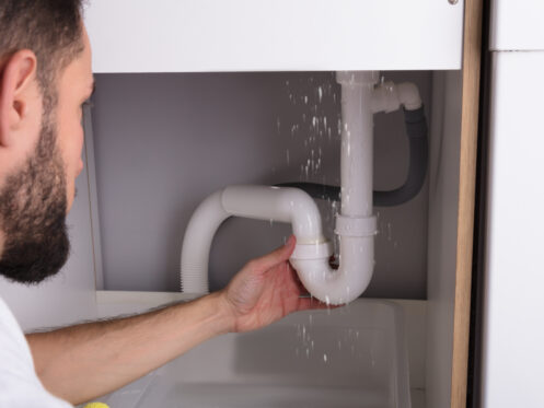 Man looking at a leaking sink pipe in a kitchen
